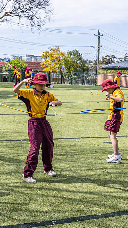 Christ the King North Rocks students playing on outdoor sports field. They are hula-hooping.